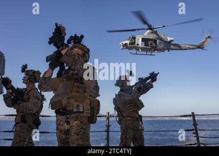 Un hélicoptère UH-1Y Venom du corps des Marines assure la sécurité alors que les Marines avec la force de raid maritime, 31st Marine Expeditionary Unit, effectuent une visite, un embarquement, une perquisition et une formation de saisie à bord de l'USS Hopper (DDG 70), Carrier Strike Group 1, au large des côtes d'Okinawa, Japon, le 8 décembre 2023. VBSS fait partie des opérations d'interception maritime qui visent à retarder, perturber ou détruire les forces ennemies ou les approvisionnements dans le domaine maritime. La 31e MEU, la seule MEU du corps des Marines déployée en continu vers l’avant, fournit une force flexible et létale, prête à effectuer un large éventail d’opérations militaires en tant que PRE Banque D'Images