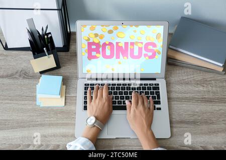 Gain de bonus. Femme utilisant un ordinateur portable à la table en bois, vue au-dessus. Illustration de la chute de pièces de monnaie et de mot sur l'écran de l'appareil Banque D'Images