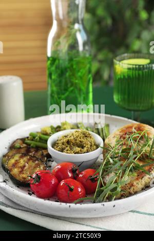 Poulet savoureux, légumes à l'estragon et sauce pesto sur table verte, gros plan Banque D'Images