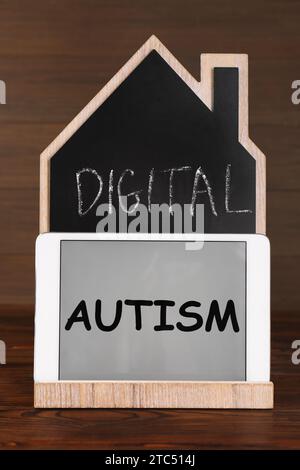 Tableau noir en forme de maison et tablette avec phrase Digital Autism sur la table en bois. Comportement addictif Banque D'Images