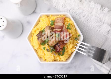 Semoule de maïs cuite avec bacon, champignons et microgreens dans un bol sur une table en marbre blanc, vue de dessus Banque D'Images