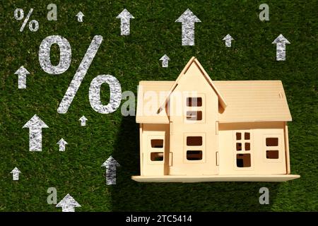 Hausse du taux hypothécaire illustrée par des flèches ascendantes et des signes de pourcentage. Modèle de maison sur herbe verte, vue de dessus Banque D'Images