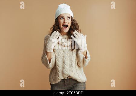 Bonjour l'hiver. femme élégante surprise en pull beige, mitaines et chapeau sur fond beige. Banque D'Images