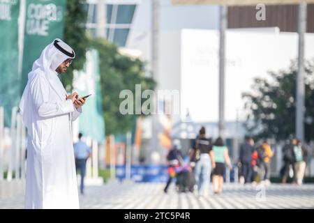 Dubaï, Émirats arabes Unis. 11 décembre 2023. Un homme regarde son téléphone portable sur le terrain de la COP28 de la Conférence des Nations Unies sur les changements climatiques. Les principaux thèmes de la conférence des Nations unies sur le climat de cette année incluent le financement des dommages causés par le changement climatique. Crédit : Hannes P. Albert/dpa/Alamy Live News Banque D'Images