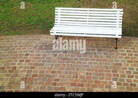 Banc en bois de couleur blanche sur le chemin pavé en pierre dans un jardin Banque D'Images