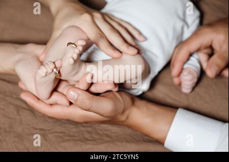 Maman et papa tiennent les jambes de leur enfant, anneaux de mariage en or sur leurs doigts, photo de famille. Banque D'Images