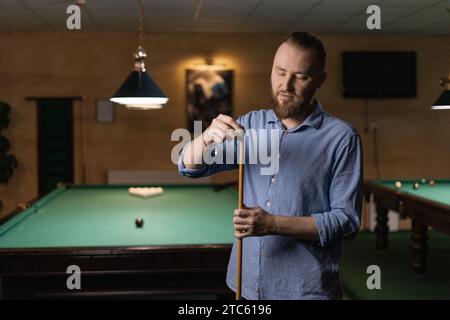 Joueur de snooker masculin se prépare à jouer au billard en frottant sa queue avec de la craie pour l'empêcher de glisser. Banque D'Images