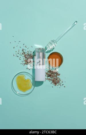 Une bouteille cosmétique est placée au centre du cadre, entourée de fleurs de lavande séchées et de miel dans une boîte de Pétri sur fond bleu. Cosmétiques Banque D'Images