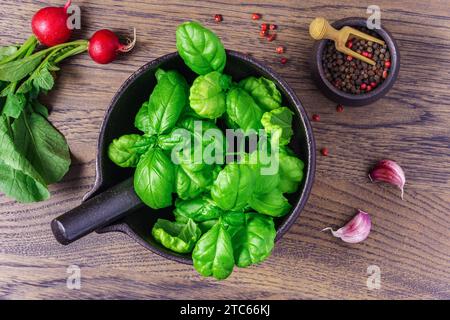 Feuilles de basilic dans un grand mortier en fonte sur la table de la cuisine, vue de dessus Banque D'Images