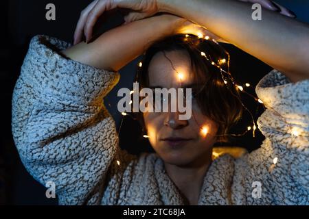 Une femme est décorée avec des lumières de Noël brillantes tenant ses mains au-dessus de sa tête. Banque D'Images