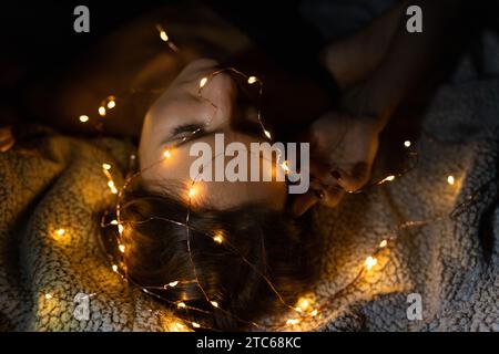 Femme couchée avec ses yeux fermés et de nombreuses lumières de fée incandescentes Banque D'Images