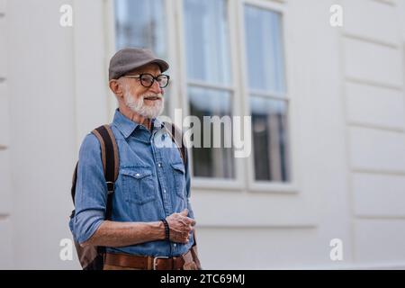 Portrait de bel homme senior dans la ville. Homme indépendant âgé avec sac à dos visitant la nouvelle ville. Voyages en voyage et en solo à la retraite. Banque D'Images