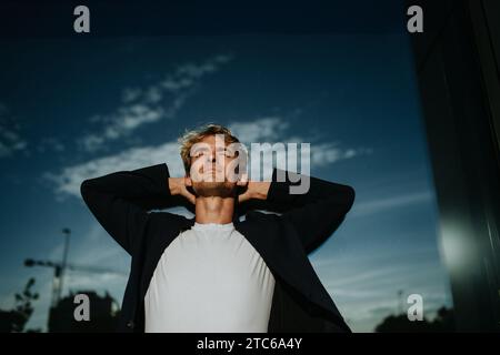 Portrait de bel homme mûr avec les cheveux blonds et les yeux fermés, debout à l'extérieur devant le mur réfléchissant. Banque D'Images