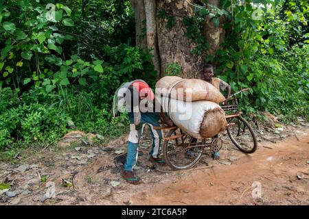 Les gens d'Afrique dans un endroit éloigné sur la route sale, les marchandises de soin sur les motos après avoir traversé la rivière, les vélos et leurs têtes, la vie photographie de rue Banque D'Images