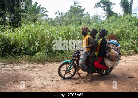Les gens d'Afrique dans un endroit éloigné sur la route sale, les marchandises de soin sur les motos après avoir traversé la rivière, les vélos et leurs têtes, la vie photographie de rue Banque D'Images
