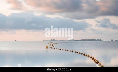 Une chaîne de bouées, s'étendant à l'horizon d'un très calme, miroir comme la mer, par un matin d'été tranquille, dans la Méditerranée. Le ciel est orange Banque D'Images