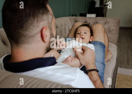 Père jouant avec bébé souriant sur le canapé à la maison Banque D'Images