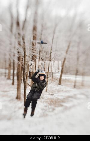 Garçon chevauchant la tyrolienne à travers la forêt d'hiver enneigée Banque D'Images