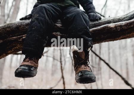 Les jambes de l'enfant pendent de la branche d'arbre portant des bottes d'hiver Banque D'Images