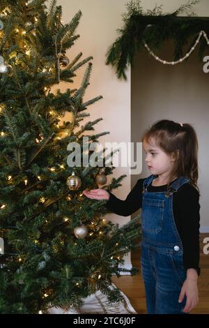 Jeune fille décorant le vrai arbre de noël avec des lumières et des ornements Banque D'Images