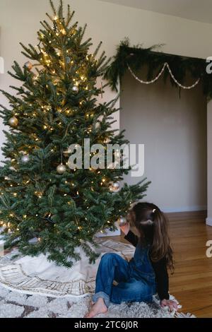 Petite fille décorant le vrai arbre de noël avec des lumières et des ornements Banque D'Images