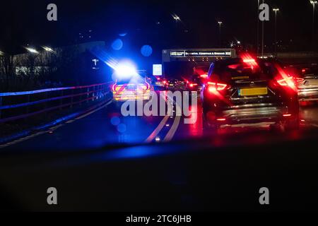 Voiture de police avec des feux clignotants bleus la nuit répondant à une urgence et rejoignant la circulation dense sur l'autoroute M8 via la jonction 15 Glasgow Écosse, Royaume-Uni Banque D'Images