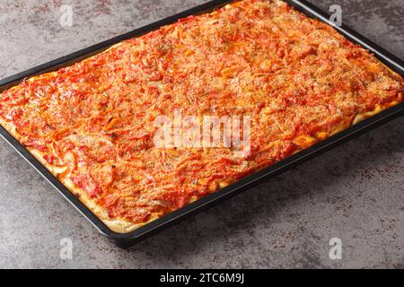 Sfincione pizza sicilienne la plus populaire un pain plat épais assaisonné avec de la sauce tomate, anchois et fromage closeup sur la plaque de cuisson sur la table. Ho Banque D'Images