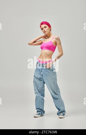 jeune femme attrayante avec les cheveux roses et les tatouages dans le crop top élégant posant sur fond gris Banque D'Images