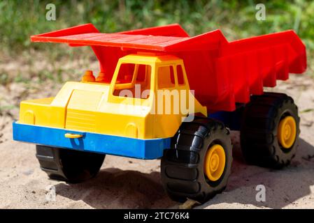 Un camion jouet en plastique en rouge, jaune et bleu sur terre. Le camion est une benne basculante qui peut transporter du sable. Banque D'Images