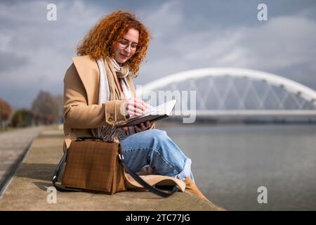 Femme caucasienne au gingembre avec des taches de rousseur et des cheveux bouclés est relaxante et lit un livre. Banque D'Images