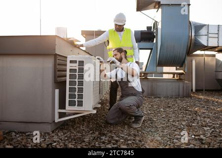 Divers travailleurs de l'usine réparant le climatiseur sur le toit Banque D'Images