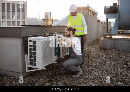 Divers travailleurs de l'usine réparant le climatiseur sur le toit Banque D'Images