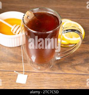 Thé noir dans une tasse en verre à double fond avec du citron et du miel. Thé pour rhumes. Banque D'Images