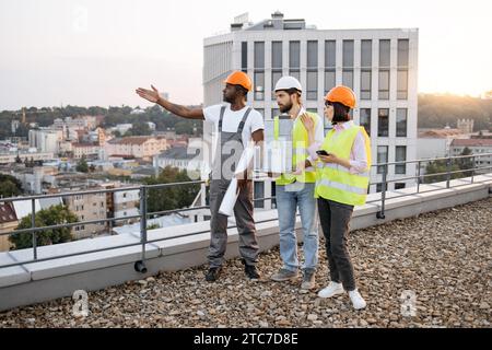 Architectes multiculturels avec équipement travaillant sur le toit Banque D'Images