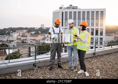 Architectes multiculturels avec équipement travaillant sur le toit Banque D'Images