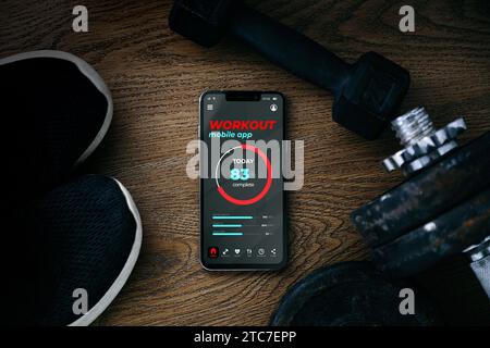 Application de formation sur l'écran du téléphone portable. Vue de dessus des haltères de fitness, des baskets et un smartphone montrant une application de santé et d'entraînement. Concept de WEL Banque D'Images