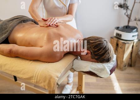 Client masculin recevant un massage du dos d'un thérapeute dans un hôtel spa moderne Banque D'Images