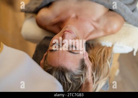 Vue aérienne d’une femme recevant un massage de la tête dans un spa avec les mains du thérapeute sur la tête Banque D'Images