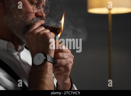 Homme barbu allumant un cigare à l'intérieur, gros plan. Espace pour le texte Banque D'Images