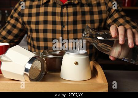 Préparer du café. Homme versant de l'eau dans le pot de moka à la table à l'intérieur, closeup Banque D'Images