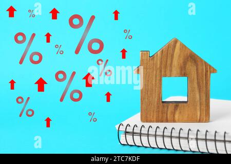 Hausse du taux hypothécaire illustrée par des flèches ascendantes et des signes de pourcentage. Modèle de maison et cahier sur fond bleu clair Banque D'Images