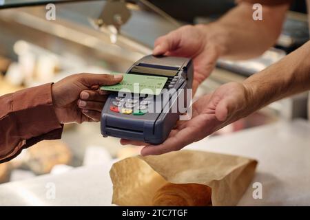 Client féminin inconnu payant pour sa commande avec carte de crédit, caissier masculin tenant la machine de carte Banque D'Images