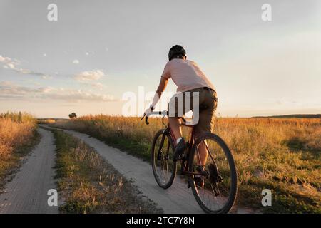 Cycliste roulant sur un sentier dans le champ sur vélo de gravier au coucher du soleil. Concept de voyage et de mode de vie actif. Banque D'Images