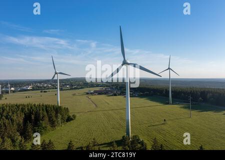 Trois éoliennes dans un champ avec en toile de fond une forêt et un petit village. Image conceptuelle des énergies renouvelables Banque D'Images