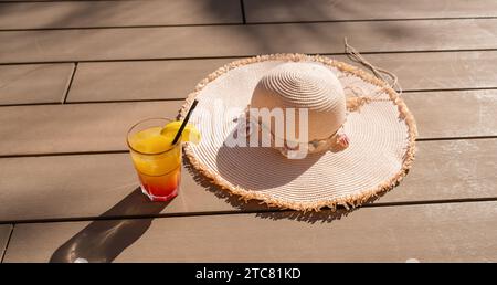 Cocktail d'été avec chapeau de paille sur une terrasse en bois, symbolisant la détente et les vibrations de vacances Banque D'Images