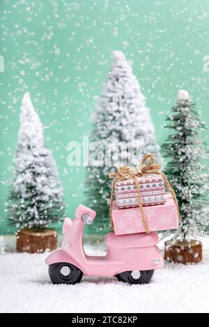 Moto jouet rose avec un cadeau de Noël à côté de sapins alors qu'il neige sur une table en bois. Concept de célébration de Noël et du nouvel an. Banque D'Images