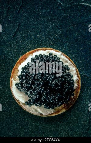 Un blini au caviar et au fromage à la crème, photographié du haut sur un fond de pierre noire Banque D'Images