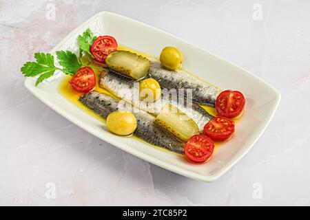 Une assiette en céramique blanche remplie de sardines marinées et de garniture fraîche. Banque D'Images