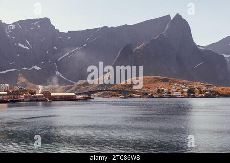 Les teintes automnales projettent une lueur chaude sur les îles Lofoten, où un pont arcade gracieusement contre les montagnes imposantes et les eaux calmes. Norvège Banque D'Images