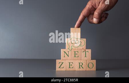 main posant des blocs en bois avec le concept zéro net des affaires et de la technologie sans carbone, empreinte carbone, fond bleu gris. Banque D'Images